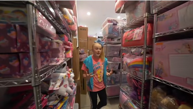 Untuk menyimpan semua merchandise bertema Jojo Siwa, salah satu kamar di rumah tersebut diubah menjadi semacam gudang penyimpanan. Kamar tersebut berisi mainan, buku, bantal dan produk-produk lainnya dengan merek Jojo Siwa. Foto: Screenshot YouTube/ Its Jojo Siwa