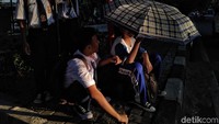Seorang pelajar sedia payung karena musim penghujan. Saat hujan tidak turun, dia pun menggunakannya untuk menghalau terik mentari.