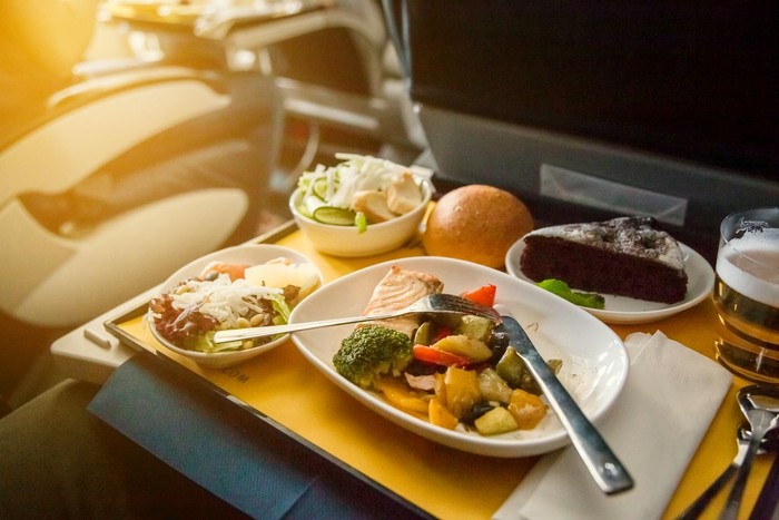 Food served on board of business class airplane on the table. Young women having a meal on board of a plane. Tray of food in the airplane. Tray of food on the plane, business class travel.