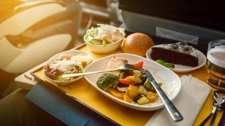 makanan di pesawat Food served on board of business class airplane on the table. Young women having a meal on board of a plane. Tray of food in the airplane. Tray of food on the plane, business class travel.