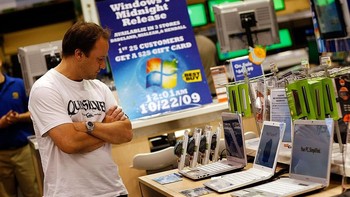 Tampak seorang konsumen mengamati laptop Windows 7, di belakangnya ada tulisan Windows 7 dirilis tengah malam ini. Foto: Getty Images
