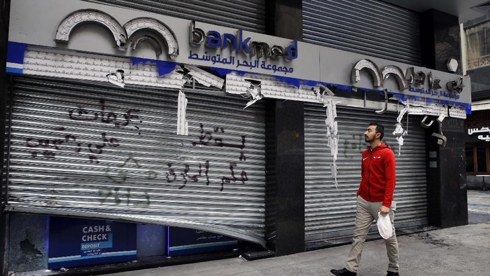 A man passes by the broken facade of the Bank MED that was smashed by anti-government protesters with a message that reads in Arabic, 