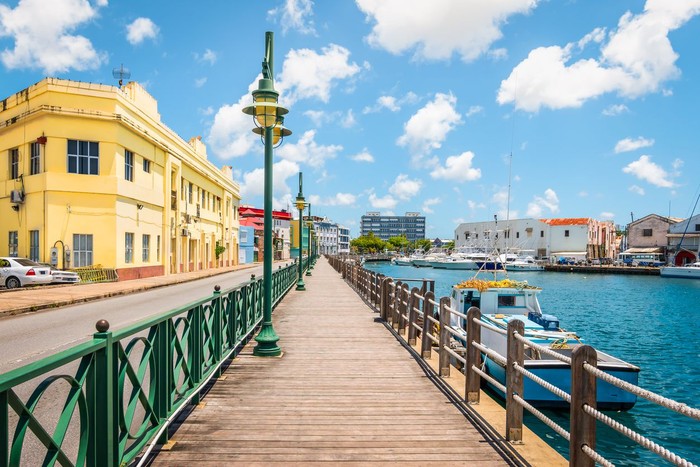 Bright image of wooden promenade at the waterfront of Bridgetown in Barbados. Colorful building against blue sky with white clouds. Boats and yachts in the harbor.