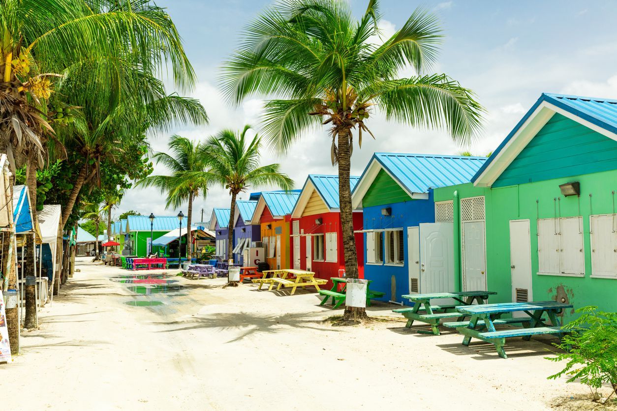 Bright image of wooden promenade at the waterfront of Bridgetown in Barbados. Colorful building against blue sky with white clouds. Boats and yachts in the harbor.