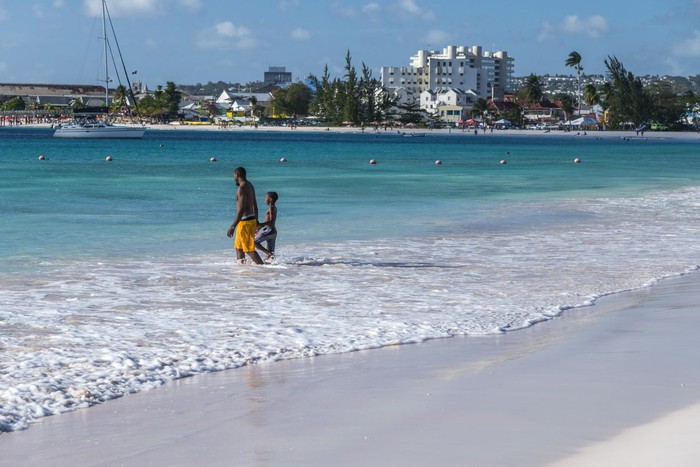 Bright image of wooden promenade at the waterfront of Bridgetown in Barbados. Colorful building against blue sky with white clouds. Boats and yachts in the harbor.