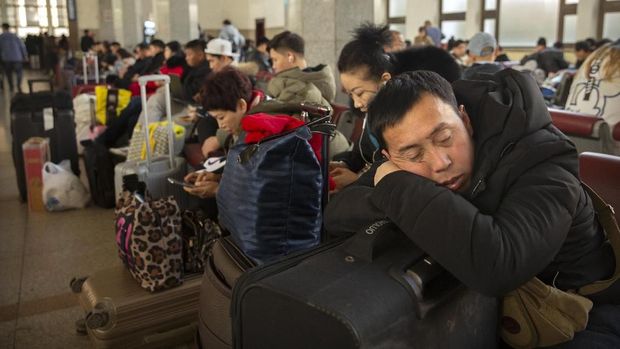 A traveler rests on his suitcase in a waiting room at the Beijing Railway Station in Beijing, Friday, Jan. 17, 2020. As the Lunar New Year approached, Chinese travelers flocked to train stations and airports Friday to take part in a nationwide ritual: the world's biggest annual human migration. (AP Photo/Mark Schiefelbein)