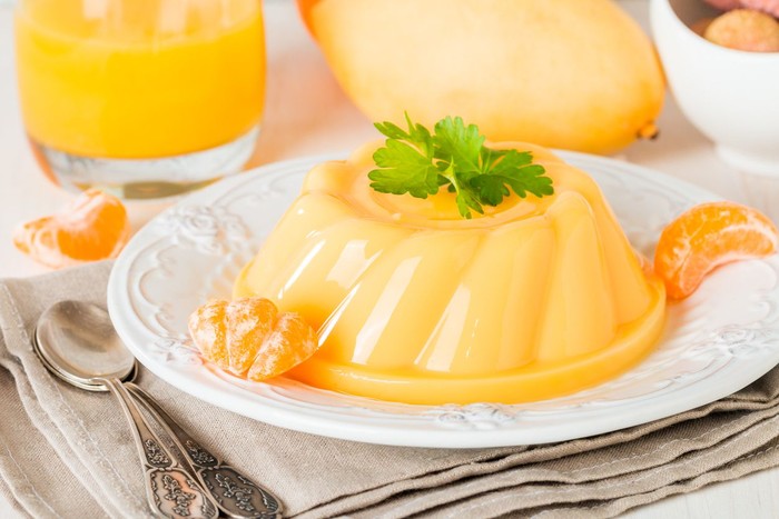 mango orange pudding on white plate with fruits on wooden table