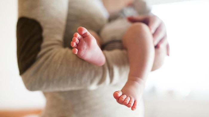 Unrecognizable mother holding her newborn baby son in her arms, close up of legs and hands.