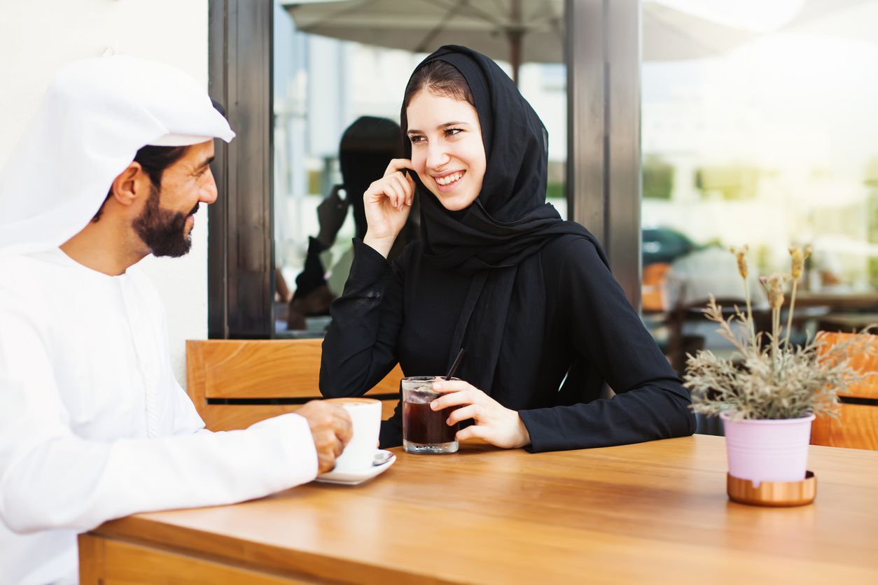 muslim customer businessman wearing black suit drinking coffee at counter with young muslim barista businesswoman background