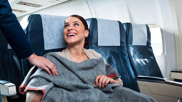 A cheerful young woman sitting on the airplane thanks an air stewardess for a blanket.