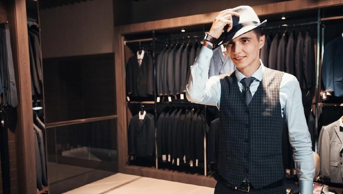 client is an elegant guy trying hat in a store by the mirror. In the background classic suits and jackets