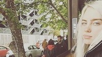 Duduk ditemani segelas air es, Billie Eilish terlihat lebih natural di foto ini. Ia tak menggunakan banyak riasan wajah. Foto: Istimewa/Instagram