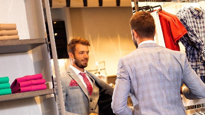client is an elegant guy trying hat in a store by the mirror. In the background classic suits and jackets