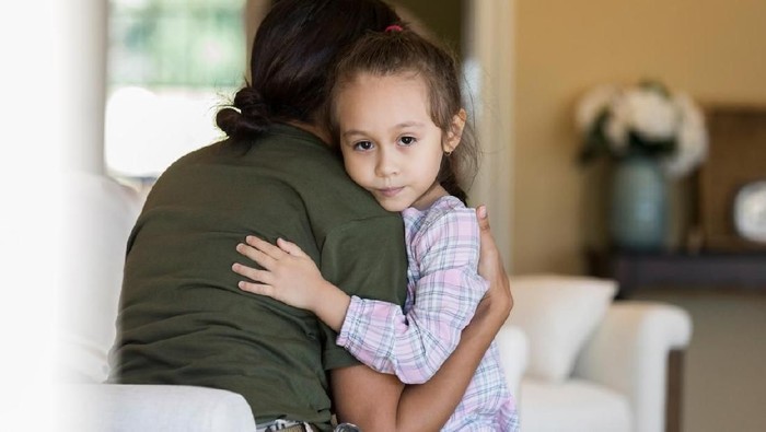1094681738 Little girl looks at the camera with a sad expression while hugging her military mom before she leaves for military deployment.