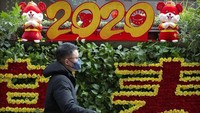 Traveler yang memakai masker melintas di depan dekorasi Imlek di Beijing, China. AP Photo/Mark Schiefelbein.