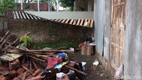 Rumahnya tampak sepi dan kurang terawat. Di halaman terdapat tumpukan genting dan kayu.