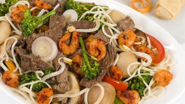 Chow mein - Chinese stir-fried noodles with beef, shrimp and vegetables on a white background. Spring rolls on the side.