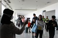 Petugas Bandara Juanda melakukan pemeriksaan suhu tubuh penumpang. 