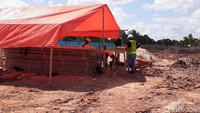 Para pekerja tengah bekerja sambil berteduh di bawah terpal oranye.