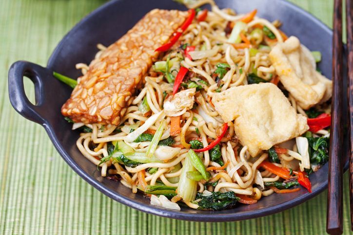 Chow mein - Chinese stir-fried noodles with beef, shrimp and vegetables on a white background. Spring rolls on the side.