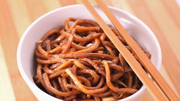 Chow mein - Chinese stir-fried noodles with beef, shrimp and vegetables on a white background. Spring rolls on the side.