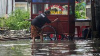 Seorang pedagang memanfaatkan air genangan banjir untuk membersihkan gerobak dagangannya di kawasan Sunter, Jakarta, Jumat (24/1/2020).