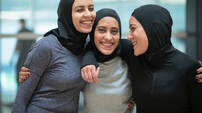 A group of Muslim women stands together smiling and embracing each other after their workout.
