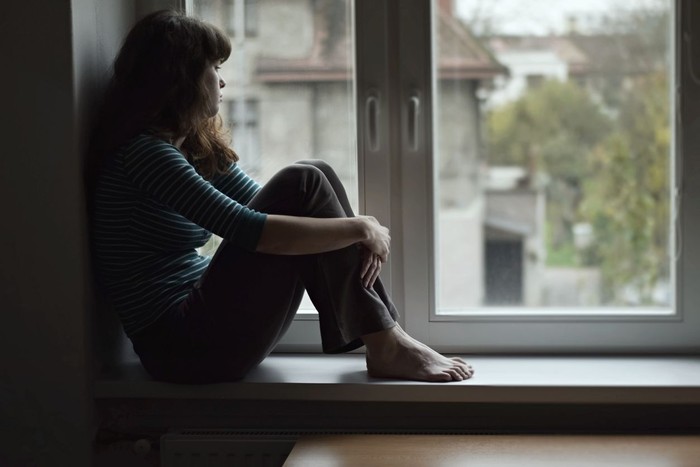 1130052240 Sad young woman sitting on the window