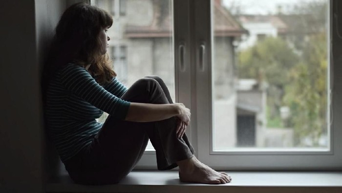Sad young woman sitting on the window