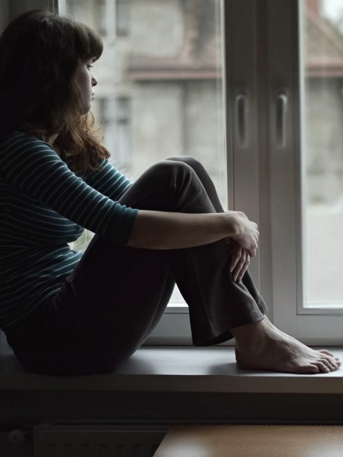 Sad young woman sitting on the window