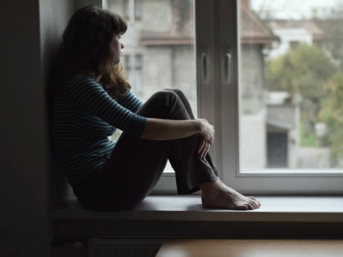 1130052240 Sad young woman sitting on the window