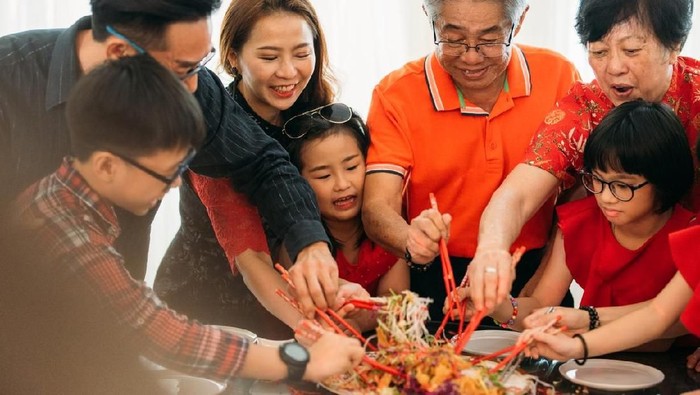 Image of Happy Family tossing of Yee Sang or YuSheng with raw salmon fillet traditional Chinese New Year prosperity delicacies.