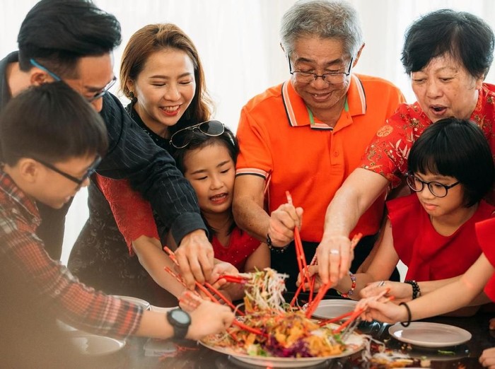 Image of Happy Family tossing of Yee Sang or YuSheng with raw salmon fillet traditional Chinese New Year prosperity delicacies.