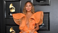 Chrissy Teigen terlihat mengenakan gaun oranye yang mengekspose kaki dan belahan dadanya. Amy Sussman/Getty Images