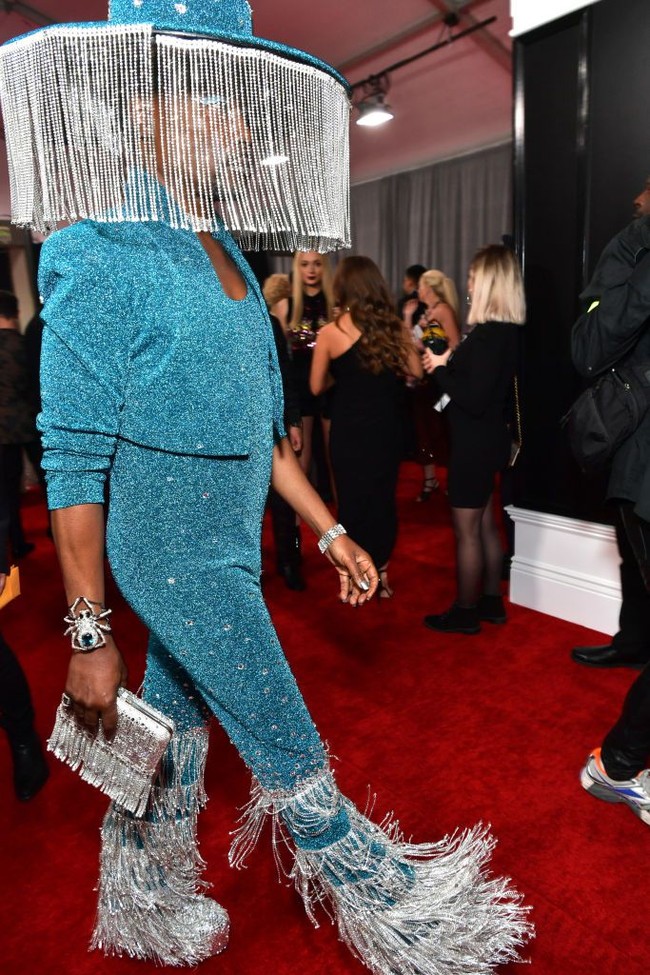 Datang ke Grammy Awards 2020, Billy Porter tampil eksentrik dengan topi bertirai. Uniknya, tirai kristal itu secara otomatis bisa terbuka sendiri. Topi birunya dengan kristalnya tersebut matching dengan busananya malam itu. Billy tampil bodysuit biru dengan bagian bawah beronce kristal. Bodysuitnya tersebut dipadankan dengan bolero senada.  Penampilannya disempurnakan dengan aksesori yang tak kalah bling-bling. Ia menggunakan sepatu tinggi perak dengan aksen kristal dan clutch kristal fringe. Foto Getty Images
