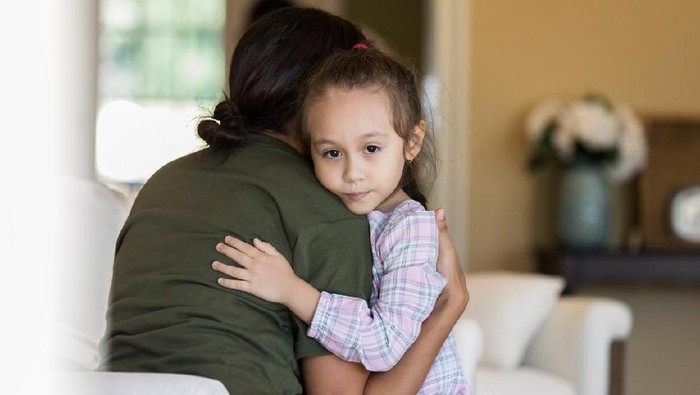 Little girl looks at the camera with a sad expression while hugging her military mom before she leaves for military deployment.