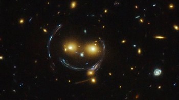 Galaksi tersenyum. Galaxy SDSS J1038+4849 dikenal juga dengan sebutan Smiley Galaxy karena tampilannya yang persis terlihat seperti wajah tersenyum yang ceria. Posisi mata dan hidung galaksi ini seolah mempertegas bentuk wajahnya, sedangkan bentuk kurva terbentuk karena pelensaan gravitasi. Foto: via Brainberries