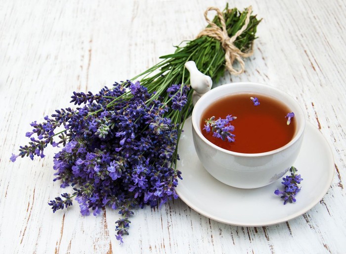 Glass cup of green camomile tea and wild herbs on the rustic wooden background. Herbal organic tea as wellness and relax concept