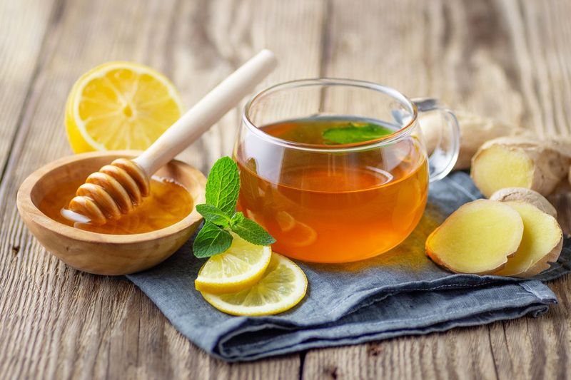 A glass cup of tea with lemon, mint, ginger and honey on wooden rustic table.