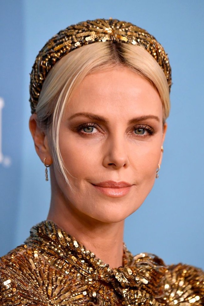 Untuk menyempurnakan gayanya, Charlize memakai bandana yang senada dengan gaunnya. Tidak ketinggalan tas Louis Vuitton Petite Malle hitam sebagai clutch. (Foto: Frazer Harrison/Getty Images)