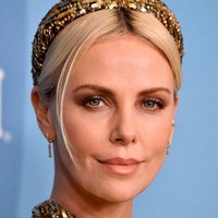 Untuk menyempurnakan gayanya, Charlize memakai bandana yang senada dengan gaunnya. Tidak ketinggalan tas Louis Vuitton Petite Malle hitam sebagai clutch. (Foto: Frazer Harrison/Getty Images)