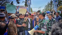 Demo diikuti puluhan orang. Tampak anggota TNI yang berjaga berusaha menenangkan warga.