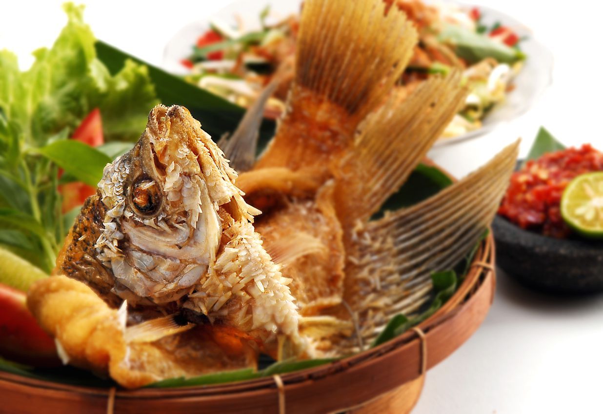Closeup of fried gourami fish meal with side salads, isolated on white background.