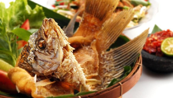 Closeup of fried gourami fish meal with side salads, isolated on white background.