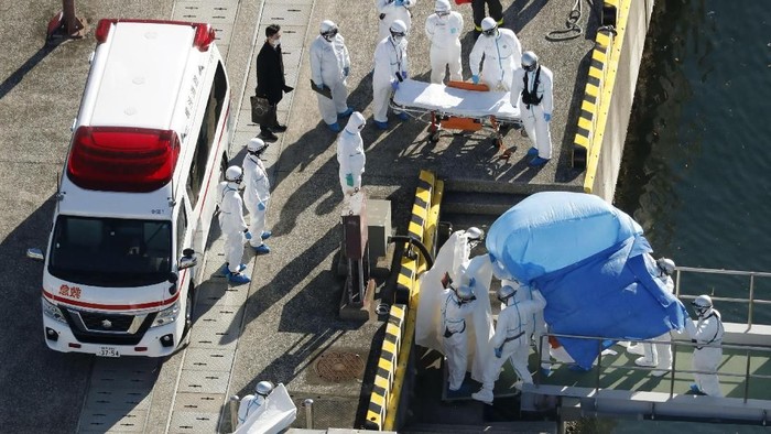 Medical workers in protective suits lead a passenger tested positive for a new coronavirus from the cruise ship Diamond Princess at Yokohama Port in Yokohama, south of Tokyo, Wednesday, Feb. 5, 2020. Japan said Wednesday 10 people on the cruise ship have tested positive for the new virus and were being taken to hospitals. Health Minister Nobukatsu Kato said all the 3,700 people and passengers on the ship will be quarantined on board for up to 14 days under Japanese law. (Hiroko Harima/Kyodo News via AP)
