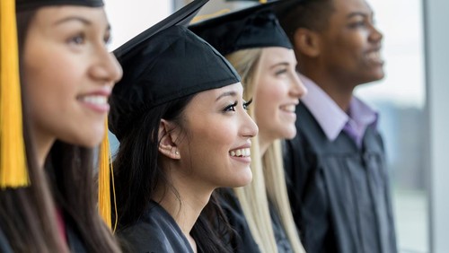 Divers group of high school of college graduates smiling during the graduation ceremony. They are standing in a row.