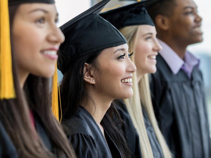 Divers group of high school of college graduates smiling during the graduation ceremony. They are standing in a row.