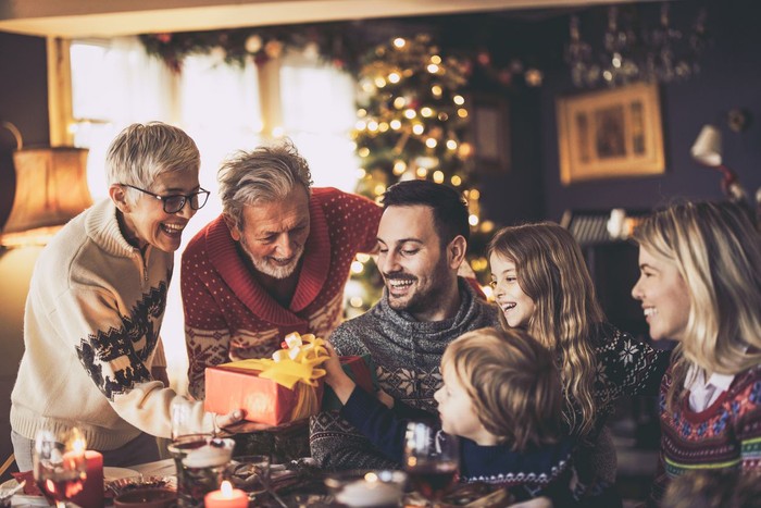 ilustrasi hadiah Happy senior grandparents giving Christmas presents to their family in dining room.