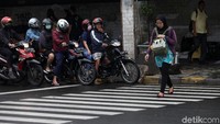 Seorang warga menyeberang jalan saat lampu traffic light menyala merah dan pengendara menghentikan laju kendaraannya.