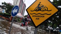 Rambu genangan air terpampang di jalan yang terendam banjir.